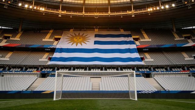 Giant uruguay flag draping across stadium seats behind center soccer goal