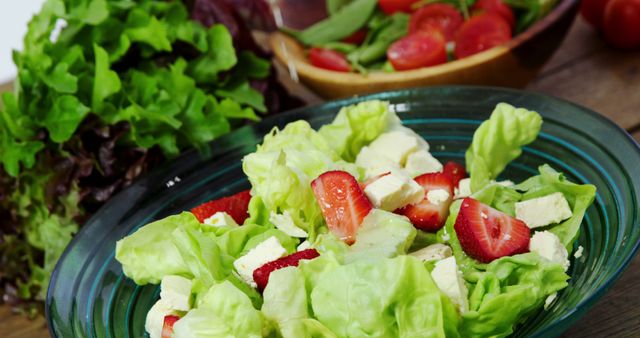 A vibrant green plate holding a fresh salad made of green lettuce, sliced strawberries, and cubes of cheese is on a wooden table. Perfect for illustrating healthy eating habits, vegetarian diet options, and organic produce. Great for use in cooking blogs, health magazines, diet books, and organic farm advertisements.