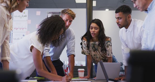 This stock photo captures a group of diverse business professionals engaged in a discussion at a contemporary office. It features men and women of different ethnic backgrounds collaborating on a project. Ideal for illustrating concepts related to business meetings, teamwork, effective communication, corporate environments, and multicultural workplaces. Perfect for use in presentations, corporate websites, marketing materials, and articles focused on business strategies, team dynamics, and workplace diversity.