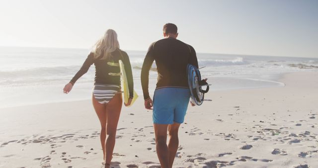 Diverse couple holding surfboards and walking on beach. Lifestyle, realxation, nature, free time and vacation.