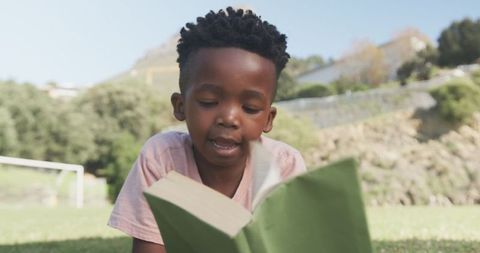 Young Boy Reading Book Outdoors on a Sunny Day