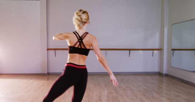 Ballet dancer in black and red practice outfit performs pirouette in dance studio. Barre and mirrors visible, emphasizing training and practice environment. Perfect for fitness blogs, dance academies, and promotional materials highlighting flexibility and grace.