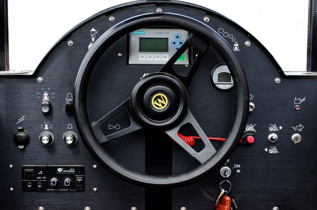 Close-up of an industrial vehicle's control panel featuring a steering wheel, various buttons, gauges, and indicators. Ideal for use in presentations about industrial machinery, vehicle technology, and equipment operation. Could be used to illustrate topics in mechanical engineering, automation, and technical training materials.