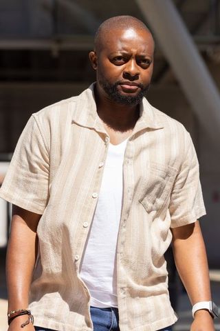 Sunlit african man walking through transit hub wearing beige shirt and smartwatch