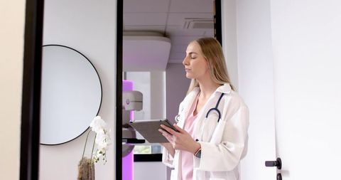 Female doctor reviewing tablet at clinic door with stethoscope and diagnostic imaging