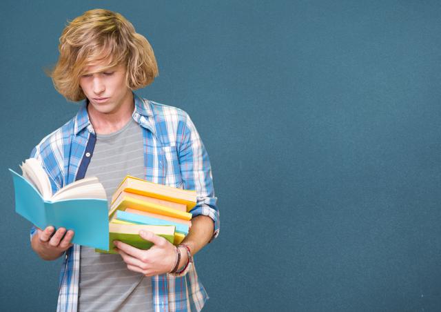 Young man concentrates on reading book while holding stack of colorful books, blue background suggesting indoor academic or educational environment. Useful for promoting education, study habits, or literacy programs.