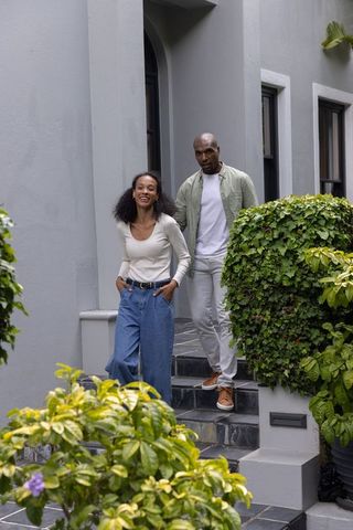 Couple walking down townhouse steps smiling, casual outdoor lifestyle among green plants