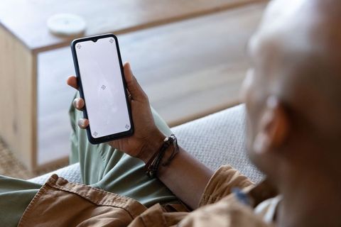 African american man holding smartphone on sofa with blank screen for app mockup