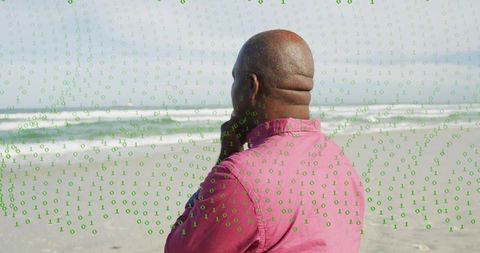 Senior man standing on beach contemplating digital future with green binary code overlay