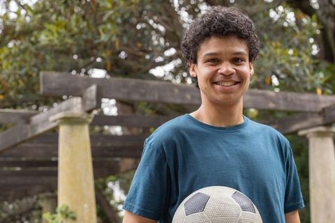 African american man smiling, holding soccer ball, standing by wooden pergola in garden