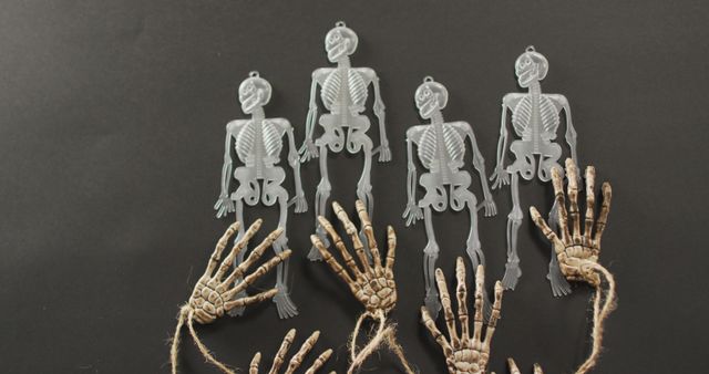 This image depicts four plastic skeleton decorations and two skeletal hands against a dark background. Perfect for use in Halloween promotions, event advertisements, party invitations, and decorations for spooky-themed events. Ideal for creating eerie atmospheres in both digital and print media.