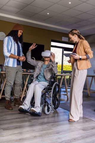 Wheelchair user experiencing virtual reality while coworkers assisting in office training