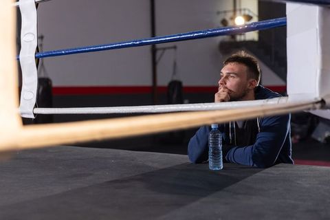 Contemplative boxer resting at ring edge leaning on hands with water bottle