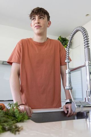 Teen standing at kitchen sink holding herbs and tomatoes, contemplative culinary lifestyle moment