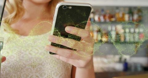Adult woman holding smartphone, scrolling social feed while sipping drink at bar