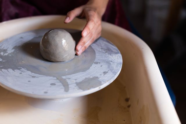 Caucasian female potter holding a ball of clay, putting it on pottery wheel. small creative business at pottery studio.