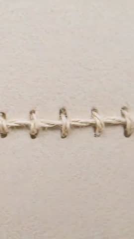 Shifting camera across twine stitch binding on beige cardstock cover