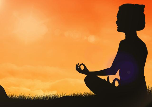 Silhouette of woman sitting for meditation on grass against orange sky