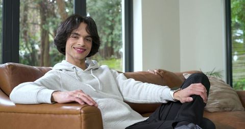 Young man relaxing on leather sofa in modern living room with greenery outside