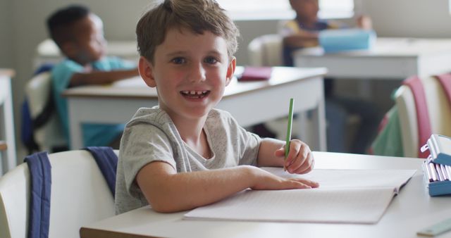 Image of happy caucasian boy sitting at desk during lesson in classroom. primary school education and learning concept.