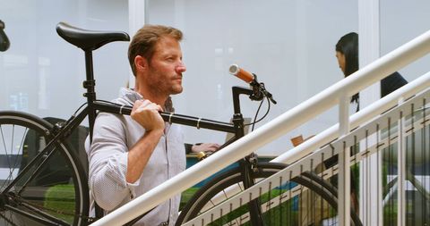 Businessman carries bicycle up stairs in modern office