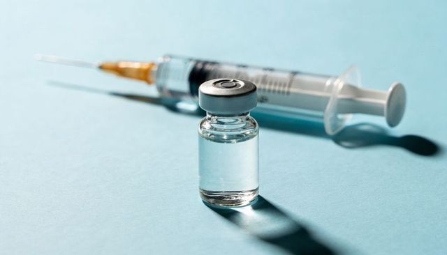 Sterile vaccine vial and syringe on blue tabletop casting sharp clinical shadows
