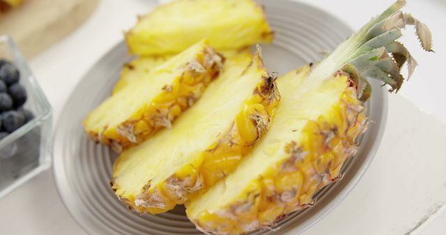 Slices of a freshly cut pineapple arranged on a plate. Perfect for use in articles about healthy eating, tropical fruits, or summer recipes. Bright yellow color emphasizes its freshness and juiciness, making it ideal for food blogs, nutrition advice, and tropical-themed websites.