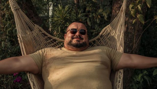 Relaxing man reclining in hammock wearing sunglasses during golden hour garden retreat