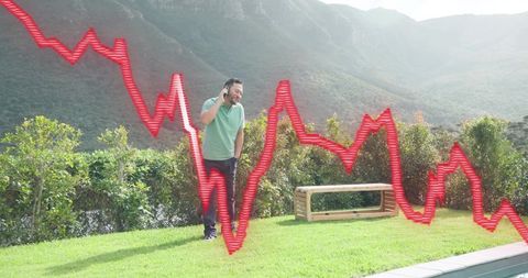 Asian man talking on phone by pool in backyard with fluctuating red market graph overlay
