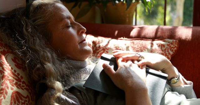 Mature woman resting on couch with sunlight streaming in, creating a peaceful and serene environment. Ideal for concepts of relaxation, stress relief, downtime, outdoor connection, wellness, or retirement.