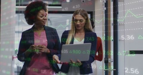 Black and Caucasian professionals walking and reviewing laptop showing stock analytics