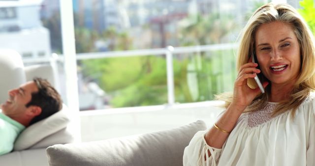 Smiling woman talking on phone while sitting on couch at home - Download Free Stock Images Pikwizard.com