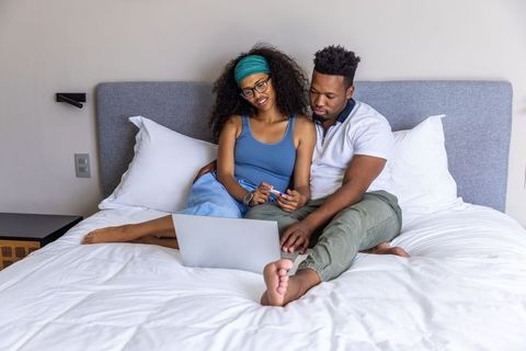 Couple relaxing on bed using laptop and credit card for online shopping at home