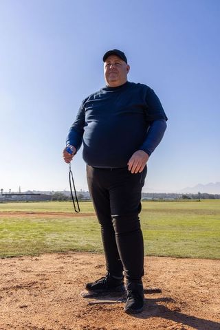 Baseball coach standing on pitcher's mound holding stopwatch during outdoor training