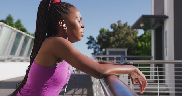 Tired african american woman wearing earphones taking a break from running on the city bridge. fitness sports and active lifestyle concept