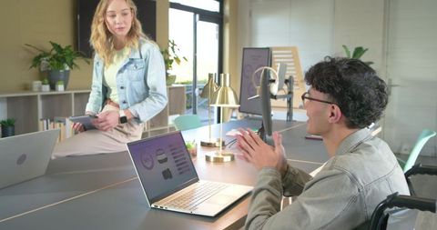 Inclusive coworking teamwork with wheelchair user presenting laptop charts in modern office