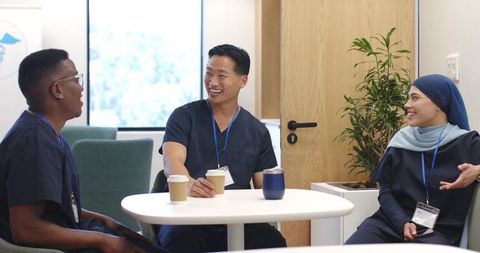 Multicultural healthcare team laughing and chatting in bright staff lounge around table