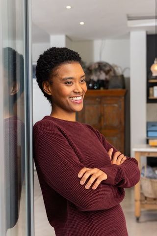 Confident african american woman leaning on glass wall smiling in modern apartment interior