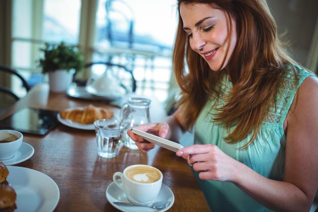 Smiling woman clicking photo of coffee from mobile phone in cafÃ©