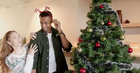 Diverse Couple Laughing by Festive Christmas Tree with Antler Headband
