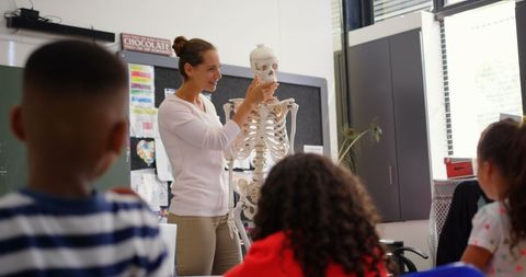 Teacher demonstrating human skeleton model to engaged students in classroom