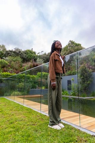 African american woman smiling by glass pool on modern deck with lush hillside backyard