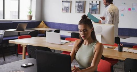 Young woman typing on laptop in modern coworking space, focused remote worker boosting productivity