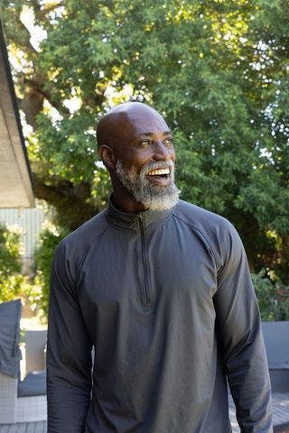 Senior african american man smiling on home patio wearing gray pullover in sunlit garden