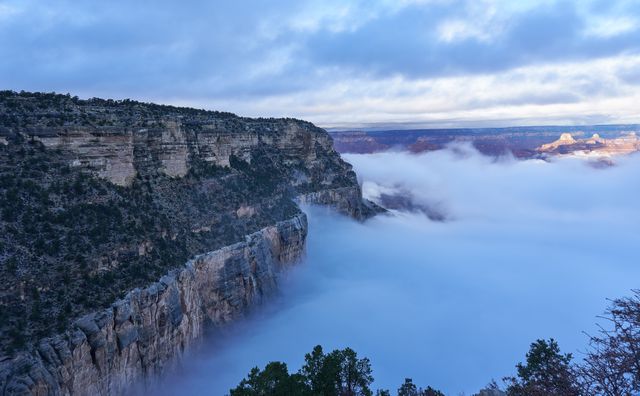 Dramatic view of the Grand Canyon shrouded in mist on a cloudy day with its majestic cliffs rising through the atmospheric fog. Ideal for use in travel guides, nature magazines, promotional materials for tourism, and landscape photography showcases.