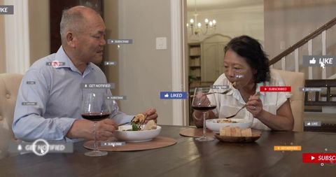 Mature couple sharing dinner with wine and floating social media like subscribe icons