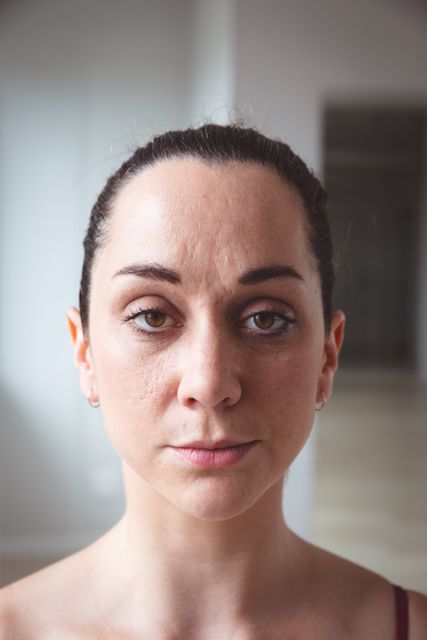 Caucasian female ballet dancer standing in a bright ballet studio, looking directly at the camera with a focused and serious expression. Ideal for use in articles or advertisements related to dance, performing arts, ballet classes, professional dancers, and the discipline and dedication required in ballet.