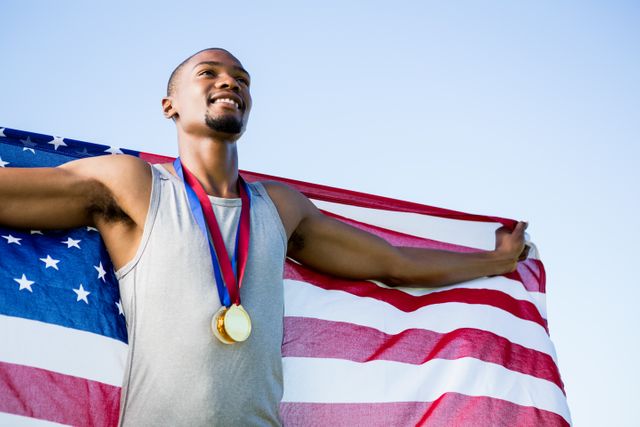 Athlete holding American flag and wearing gold medal, celebrating victory. Ideal for use in sports-related content, patriotic themes, motivational materials, and advertisements promoting fitness and success.