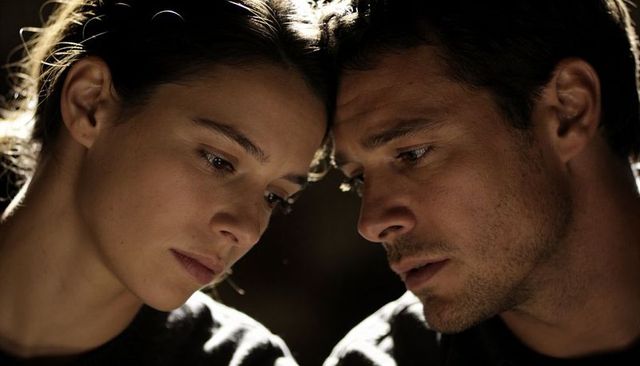Intimate closeup of couple leaning foreheads together sharing pensive moment in moody light