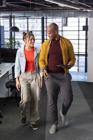 Diverse coworkers walking and collaborating with tablet in modern industrial office space